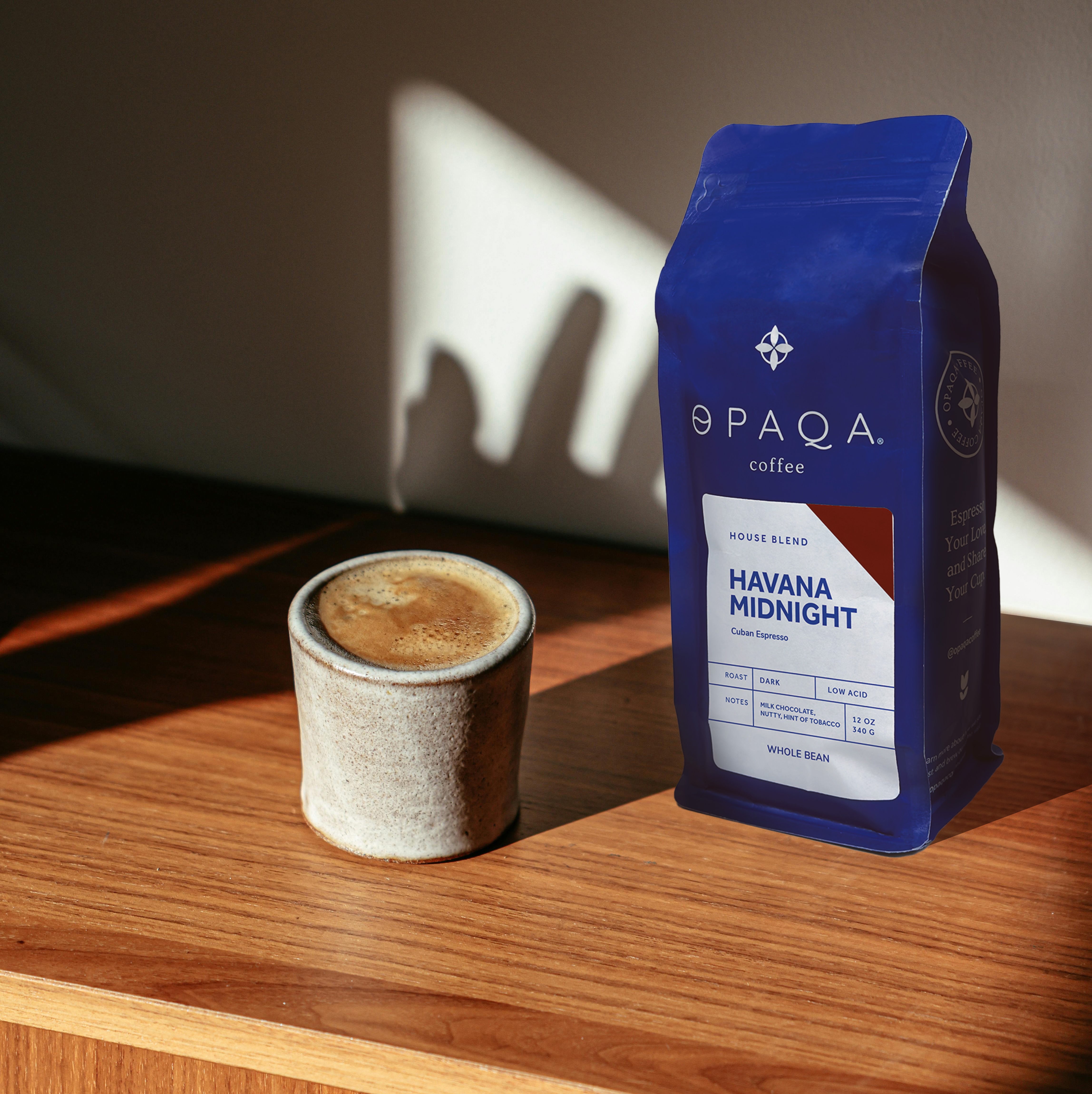 Opaqa coffee bag labeled 'Havana Midnight' next to a cup of coffee on a wooden surface.