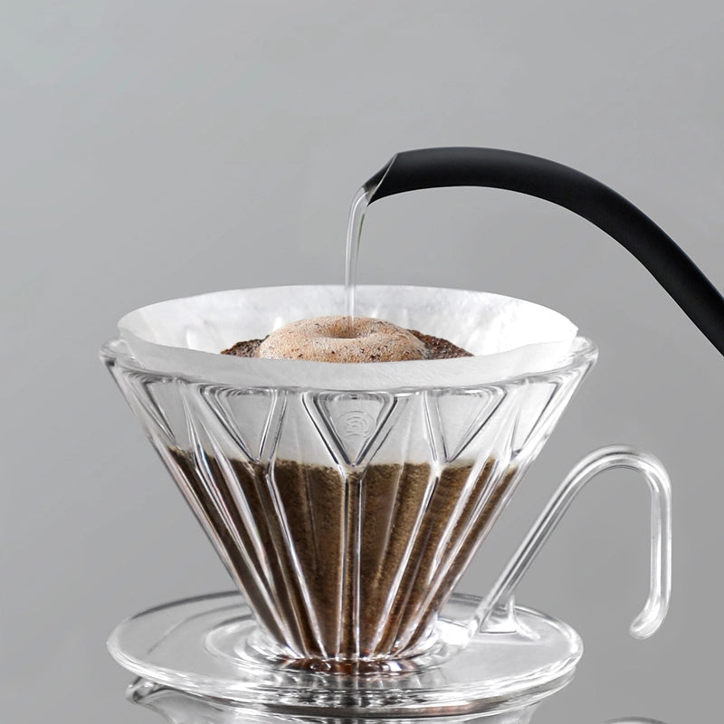 Coffee brewing process with a clear glass coffee filter and black handle on a gray background