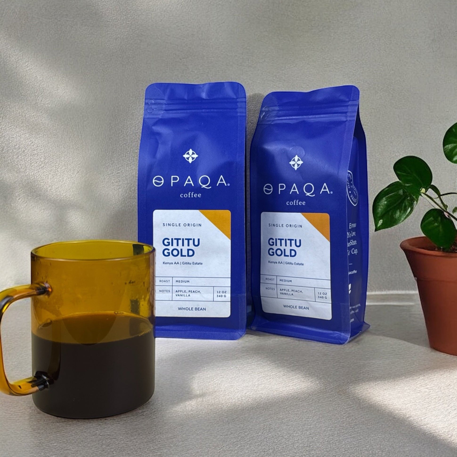 Two blue Opaqa coffee bags labeled 'Gititu Gold' on a light surface with a yellow mug and plant.