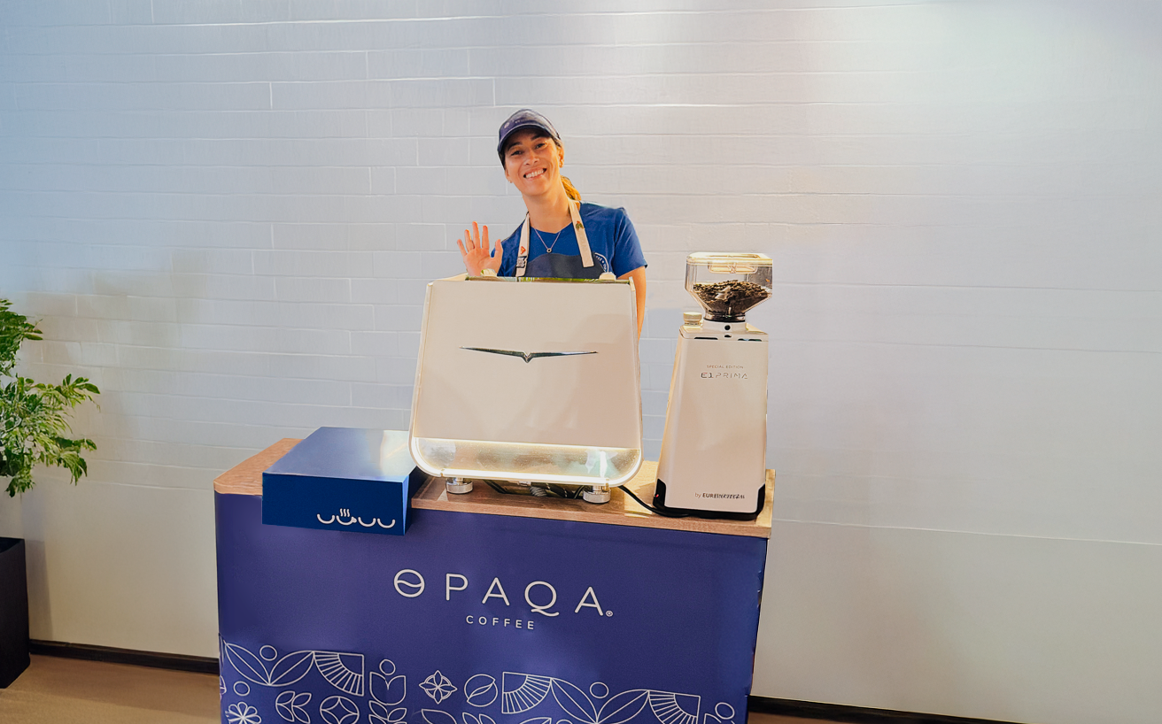 Person standing behind a branded coffee cart with 'Opaqa Coffee' on a blue cart.