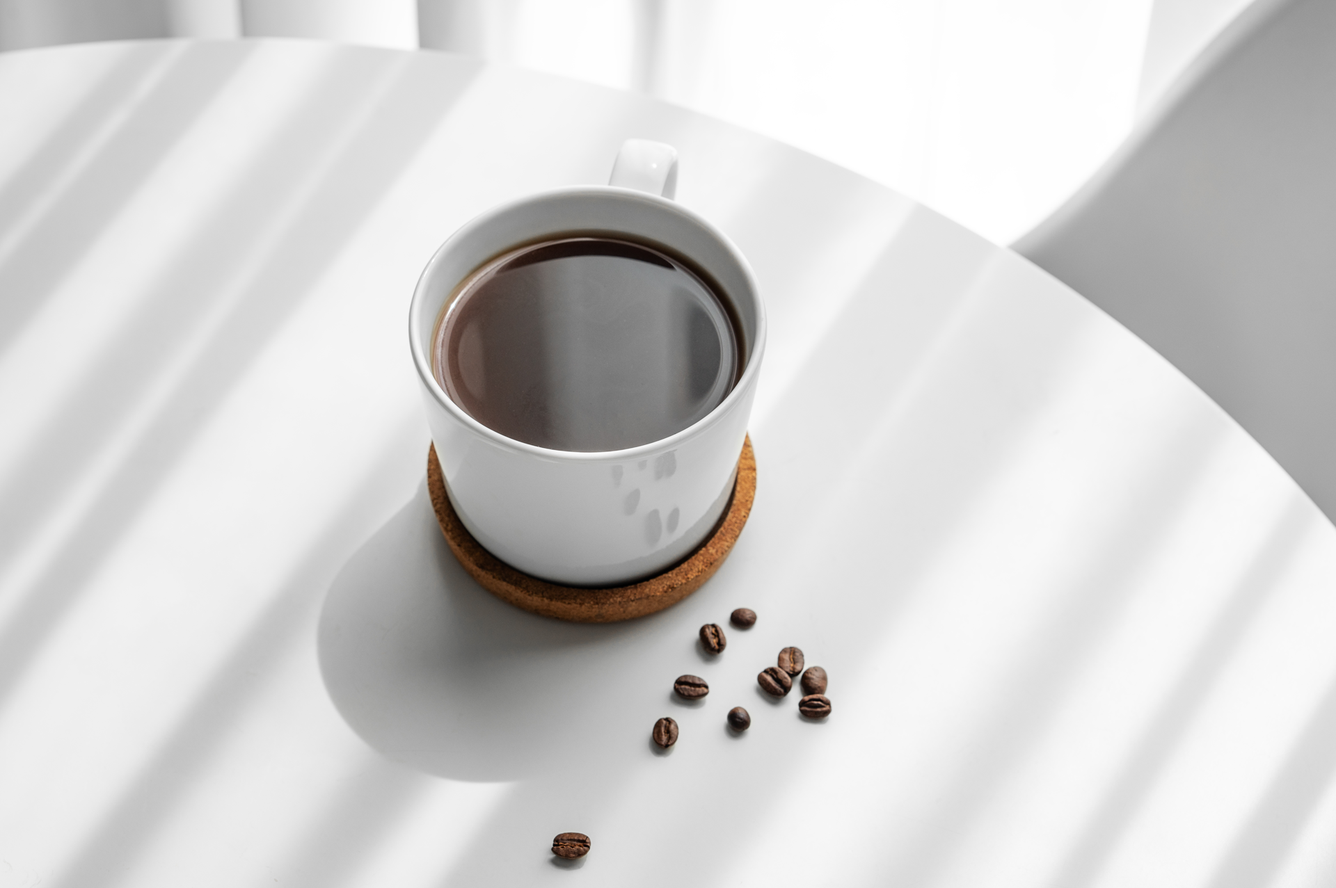 White mug with coffee and scattered coffee beans on a white surface